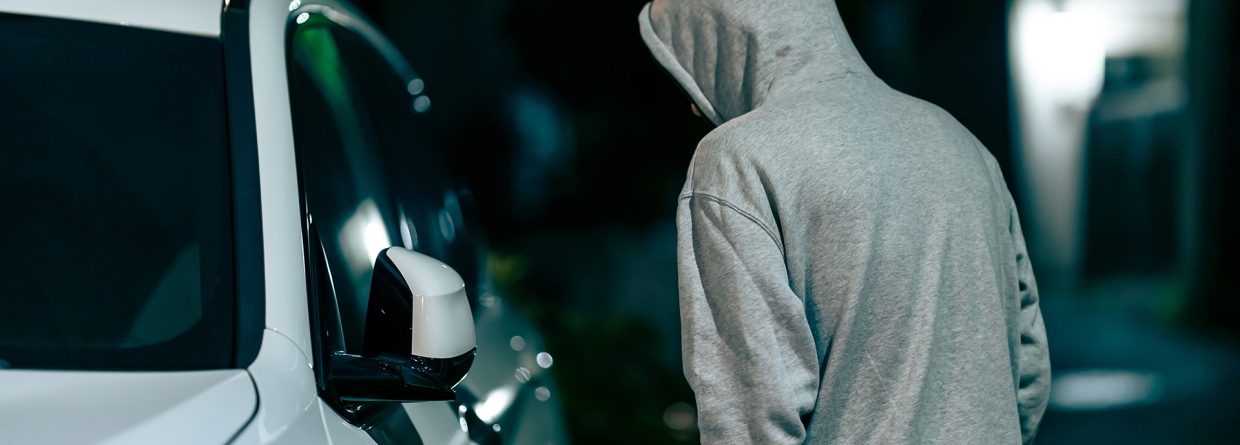 auto-inbraken; man loopt in het donker langs een witte auto en kijkt naar binnen 