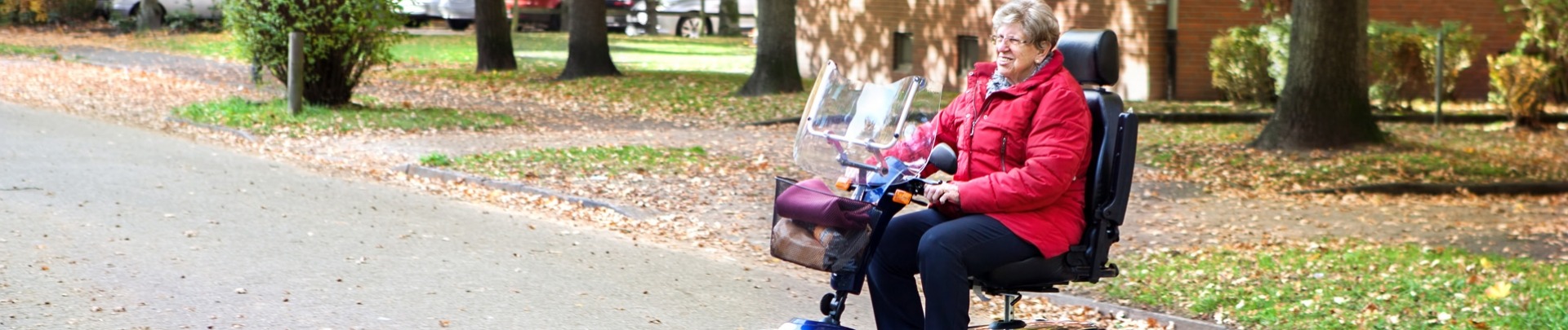 Een vrouw met een rode jas aan zit op een blauwe scootmobiel